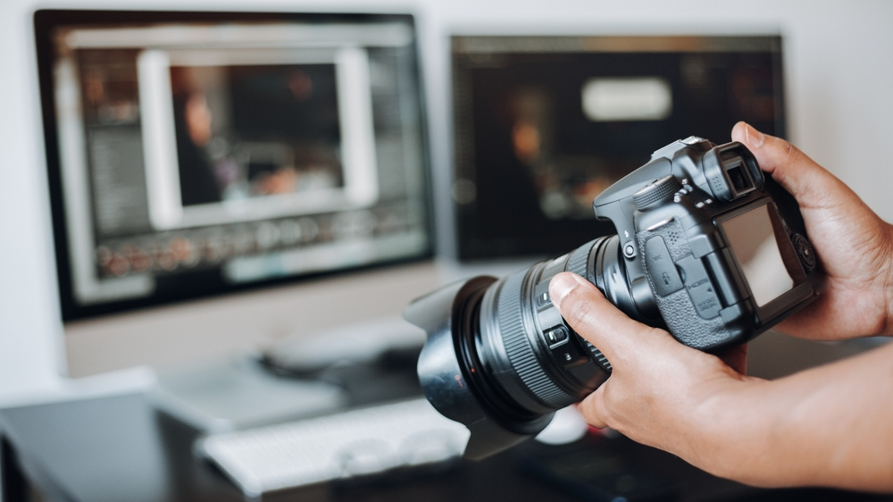 Photographer holding a camera and computer on the desk. Creating a video content for a marketing strategy.