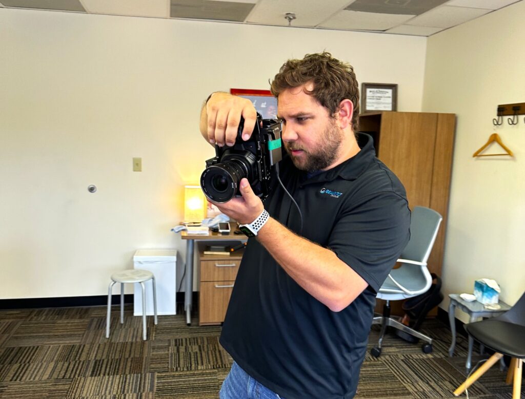 Videographer at GeauxTo Group, a digital marketing agency in New Orleans focusing intently as he operates a professional camera in an office setting.